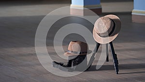 Sunlight and shadow on surface of lady hat and fedora hat hanging on camera tripod with black camera bag on wooden tiles floor in