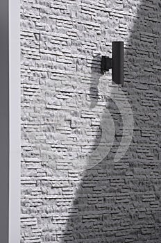 Sunlight and shadow on surface of outdoor black cylinder wall lamp on vintage white and gray ledgestone wall