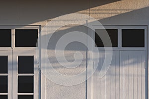 Sunlight and shadow on white wooden door and tinted glass window on gravel wall of vintage house