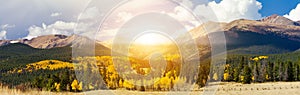 Sunlight shining over high mountain peaks and golden aspen trees in a panoramic Colorado landscape photo