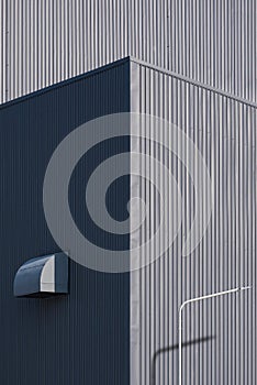 Sunlight on surface of street light post with air duct ventilation on gray corrugated metal industrial building