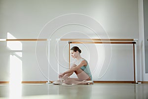 Sunlight. Tender young girl, ballerina sitting on floor and putting on pointe shoes. Training in ballet school, indoors
