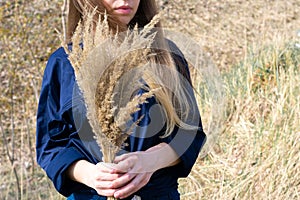 Sunlit caucasian woman with dried yellow bushgrass bunch in hands. Concept of autumn time