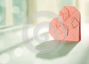 Sunlit pink origami paper heart with shadow in front