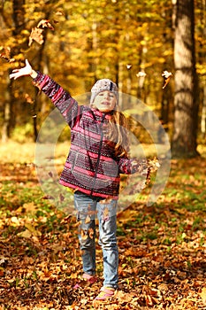 Sunlit portrait of a cheerful girl throwing leaves in  autumn park