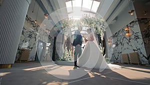 Sunlit Vows: Bride and Groom Under Floral Archway, A radiant bride and groom stand under a floral arch in a luxurious