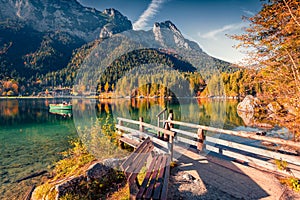 Sunny autumn view of Hintersee lake with wooden pier and fishing boat.