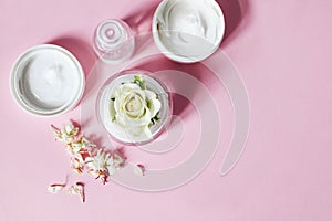 Sunny beauty composition. Closeup of skin cream, tonicum bottle, dry flowers and rose with long shadows. Pink background