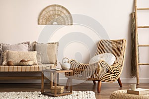 Sunny and bright composition of meditation living room interior with armchair, beige carpet, pillows, ornament and personal