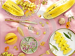 Sunny and bright open air breakfast with yellow watermelon, grape, plums and summer wild flowers decoration.