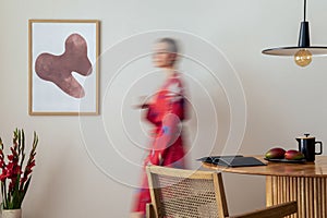 Sunny and bright space of living room with mock up poster frame, woman in red kimono, bouquet flower in vase and personal