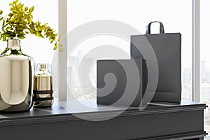 Sunny city view from room with steel vases on dark wooden surface and empty black paper bag and box. Mockup