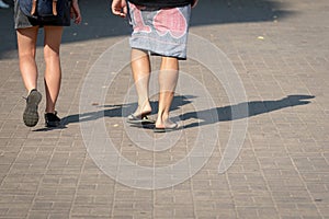 On a sunny day, a couple of people walk along the sidewalk. The human shadows are visible on the sidewalk. View from the back.