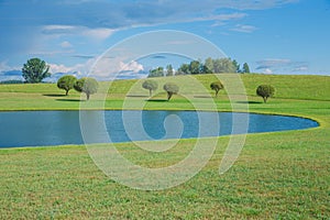 Sunny day, lake and meadow with blue sky. Treeas and clouds.