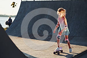 Sunny day. Little girl with scate on a ramp for extreme sports at daytime