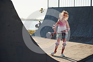 Sunny day. Little girl with scate on a ramp for extreme sports at daytime