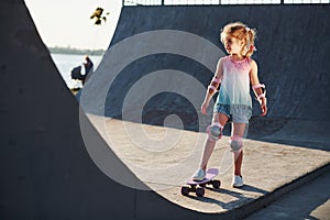 Sunny day. Little girl with scate on a ramp for extreme sports at daytime