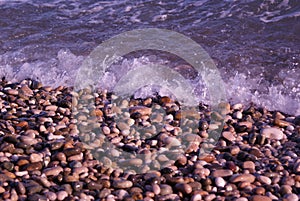 On a sunny day pebbles washed by small waves on the beach of the Black Sea