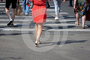 On a sunny day, pedestrians cross the street through a pedestrian crossing. There are pedestrian shadows on the street. View from
