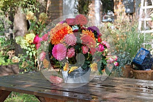 Sunny day in the village. Roses, asters, dahlia in vase in the garden on a wooden table. Veranda in the garden