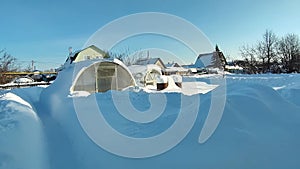 Sunny day in the winter garden. Greenhouses in snowdrifts