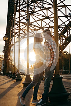Sunny emotional shot of the loving couple smiling and holding hands in the sunset near the iron archway.
