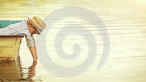 Sunny footage: a boy sits in a boat, leaning over the shipboard and putting his hands in the water