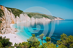 Sunny Fteri beach lagoon with rocky coastline, Kefalonia, Greece. Tourists under umbrella chill relax near clear blue photo