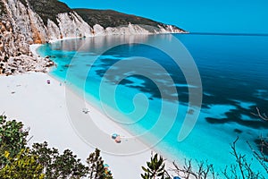 Sunny idyllic Fteri beach lagoon with limestone rocky coastline, Kefalonia, Greece. Tourists relax under umbrella near