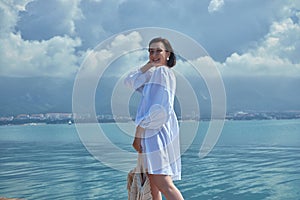 Sunny Mediterranean, young woman exudes beauty and grace against a backdrop of azure sea and coastal mountains. Brunette hair