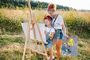 Sunny nature, mom and daughter paint a picture in a park , painting a Little Child, Child Creativity. Mother& x27;s Day.