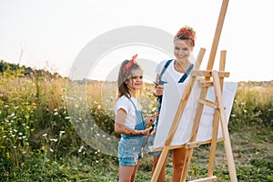 Sunny nature, mom and daughter paint a picture in a park , painting a Little Child, Child Creativity. Mother's Day.