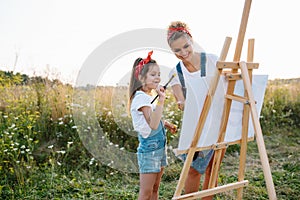 Sunny nature, mom and daughter paint a picture in a park , painting a Little Child, Child Creativity. Mother& x27;s Day.