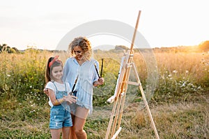 Sunny nature, mom and daughter paint a picture in a park , painting a Little Child, Child Creativity. Mother's Day.