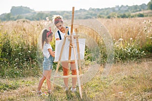 Sunny nature, mom and daughter paint a picture in a park , painting a Little Child, Child Creativity. Mother& x27;s Day.