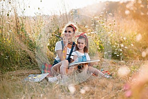 Sunny nature, mom and daughter paint a picture in a park , painting a Little Child, Child Creativity. Mother& x27;s Day.