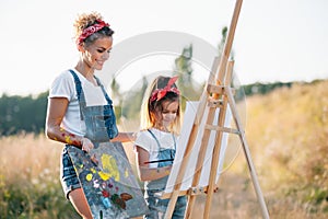 Sunny nature, mom and daughter paint a picture in a park , painting a Little Child, Child Creativity. Mother& x27;s Day.