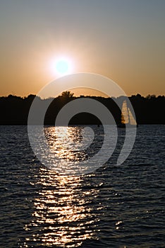 Landscape with a sailing boat on the background of the evening sun in an urban environment