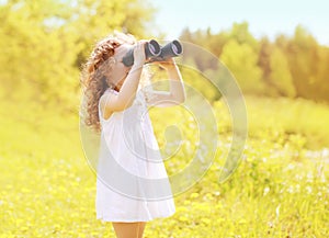 Sunny photo child looks in binoculars outdoors in warm summer