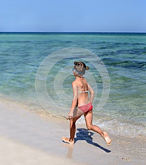 A sunny photo of a little girl in bikini running along a sea shore