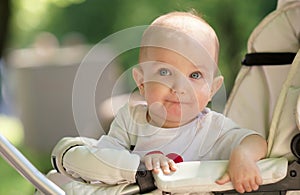 Sunny portrait of cute funny baby in white shirt sitting in baby carriage. Smiling baby with big blue eyes