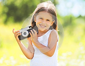 Sunny portrait of cute smiling little girl child with old camera