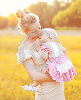 Sunny portrait of happy mom kissing baby on hands