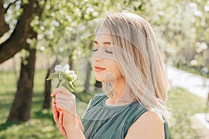 Sunny sensual portrait of a beautiful girl who sniffs an apple tree flower with her eyes closed