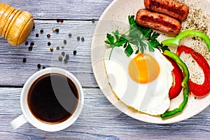 Sunny side up. Fried eggs with sausages, vegetables and cup of coffee on a light wooden table. Top view