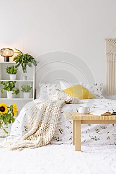 Sunny spring bedroom interior with green plants beside a bed dressed in eco cotton linen. Yellow accents