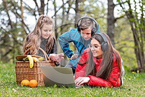 On a sunny spring day, two sisters and a brother rest on the grass next to a picnic basket in the park and watch a movie on a