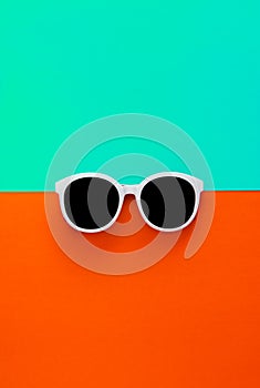 Sunny stylish white sunglasses on a bright blue-cyan and red-orange background, top view, isolated. Copy space. Flat lay