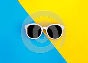 Sunny stylish white sunglasses on a bright blue-cyan and yellow-orange background, top view, isolated. Copy space. Flat lay