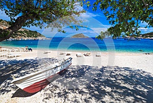 Sunny summer beach in Greece with sun beds and small boat. Agios Nikolaos Port Zakynthos island.